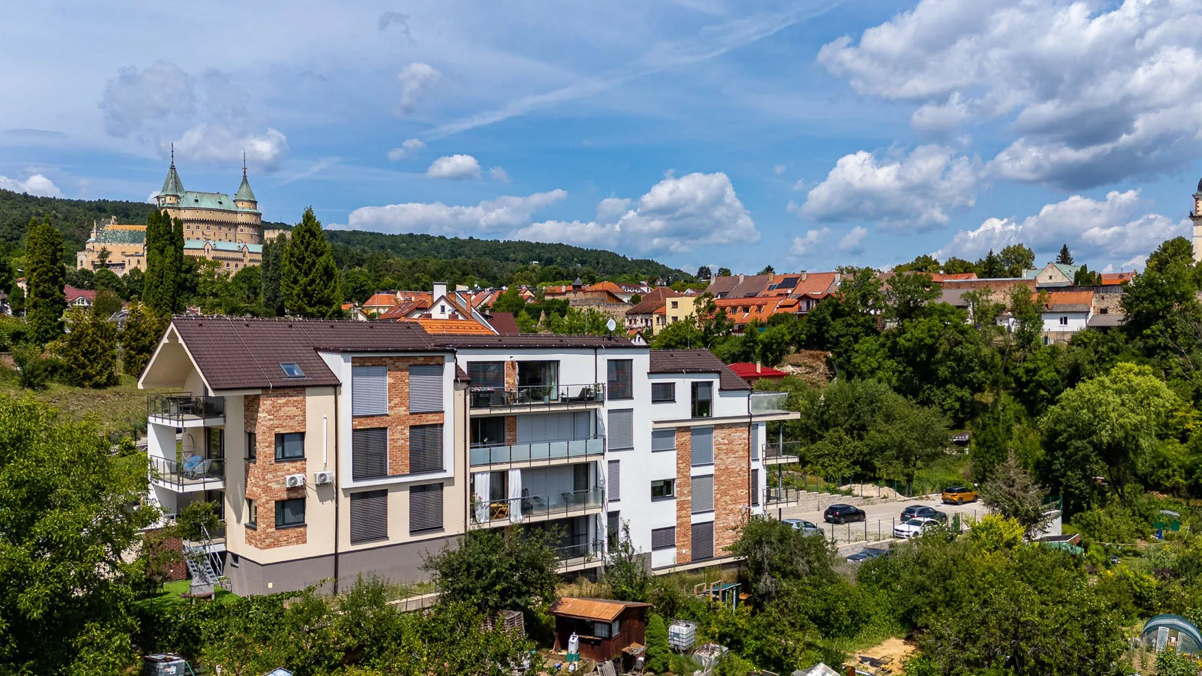 Rezidencia Pod zámkom: Bočný pohľad na apartmánový dom s balkónmi a Bojnickým zámkom na kopci.
